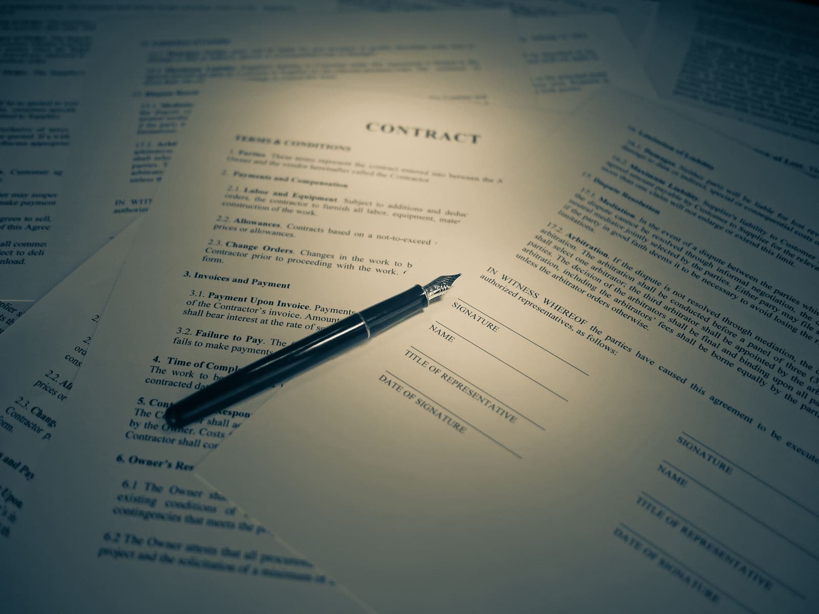 Printed contract pages fanned across a desk with a fountain pen resting on the signature, name and title of representative blocks.